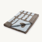 Flora – couverture en laine pliée, motif floral chocolat et ciel clair – Maison Canisya